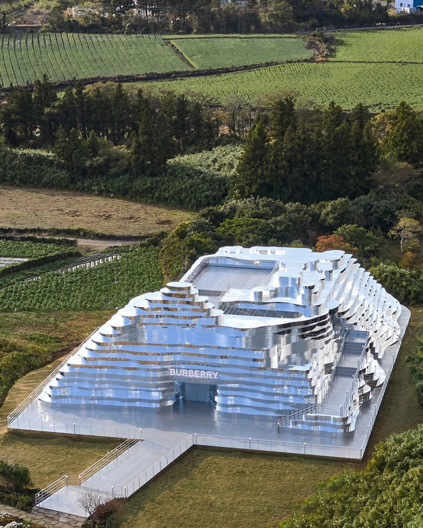 An aerial view of a mirrored, terraced experiential building set into a rural landscape